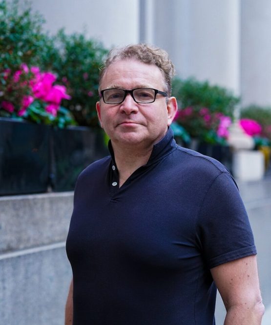 Man with glasses wearing a dark polo shirt outdoors.